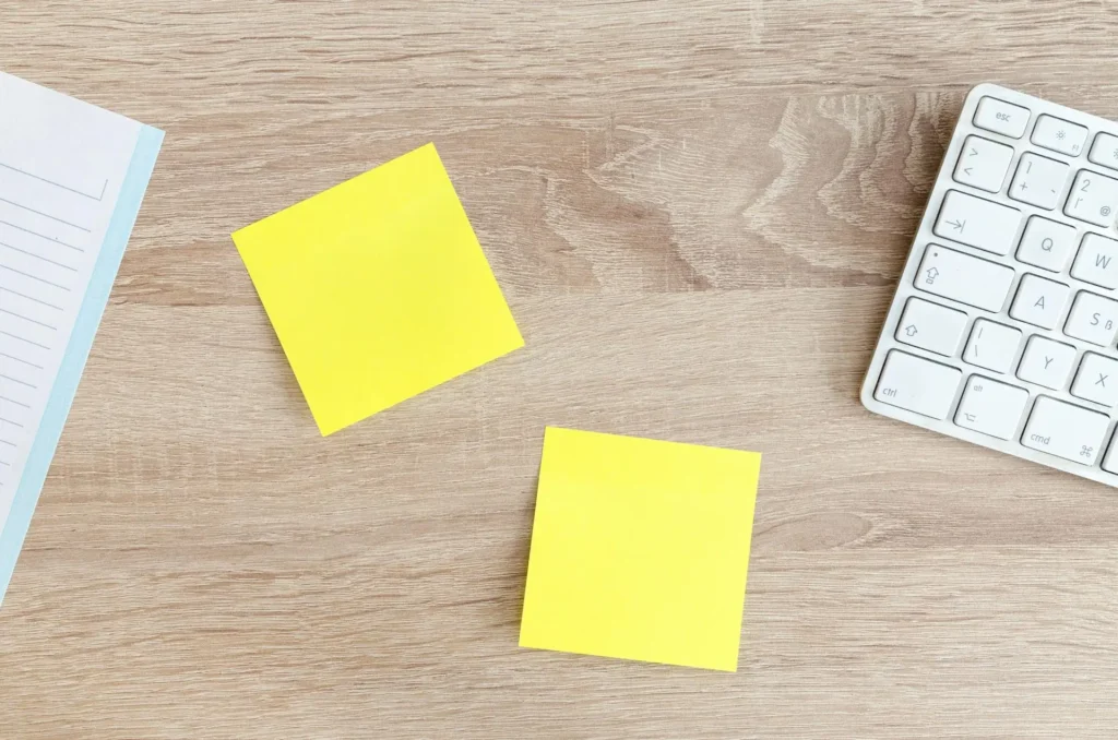 Yellow sticky notes and a keyboard on a wooden desk, symbolizing planning and organization for setting personal growth and development goals.