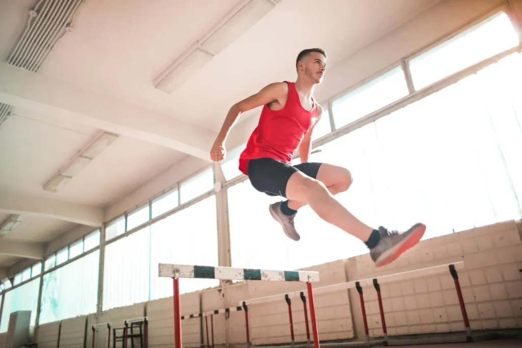 A young athlete jumping over a hurdle in a gym, symbolizing overcoming challenges.