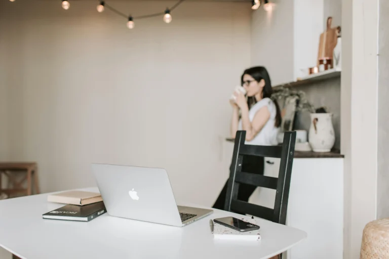 Clean workspace for effective time management with a laptop and notebook, with a woman taking a break in the background.
