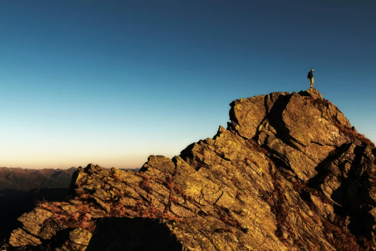A young professional standing on top of a rocky mountain peak at sunrise, symbolizing the achievement of personal growth and development goals.