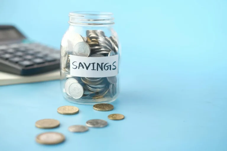 Jar filled with coins labeled 'Savings' with a calculator in the background, representing financial security and how to save money.