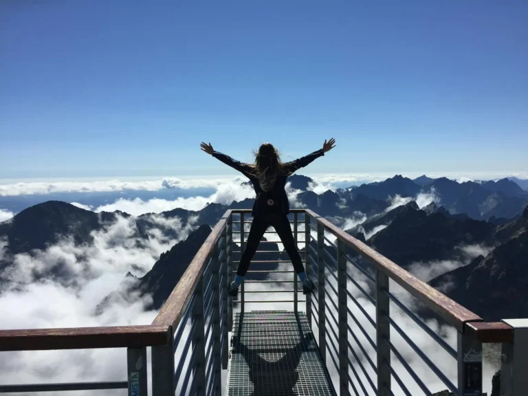 Person standing with arms raised on a mountain viewpoint, symbolizing confidence and achievement